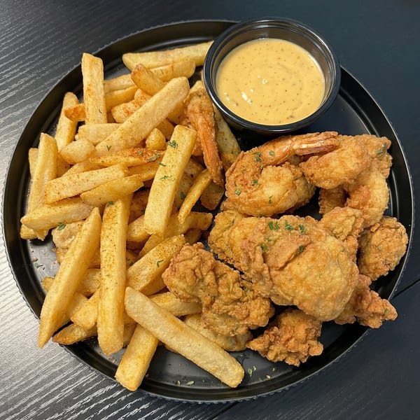 Crispy fried shrimp and chicken tenders with seasoned french fries and a side of dipping sauce.