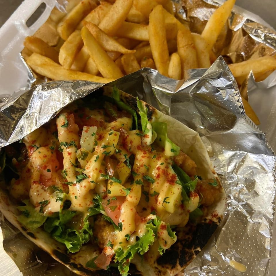 A foil-wrapped taco filled with shrimp, lettuce, and sauce, next to a container of french fries.