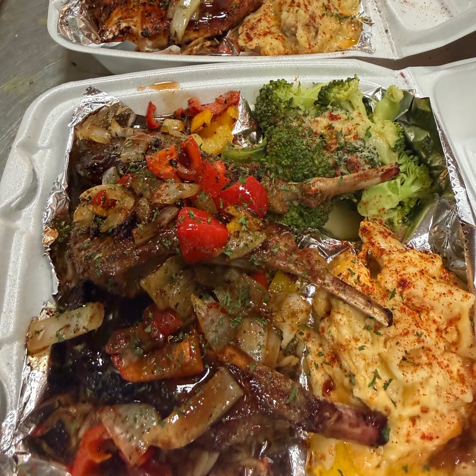 Takeout container with lamb chops, bell peppers, onions, broccoli, and macaroni and cheese.