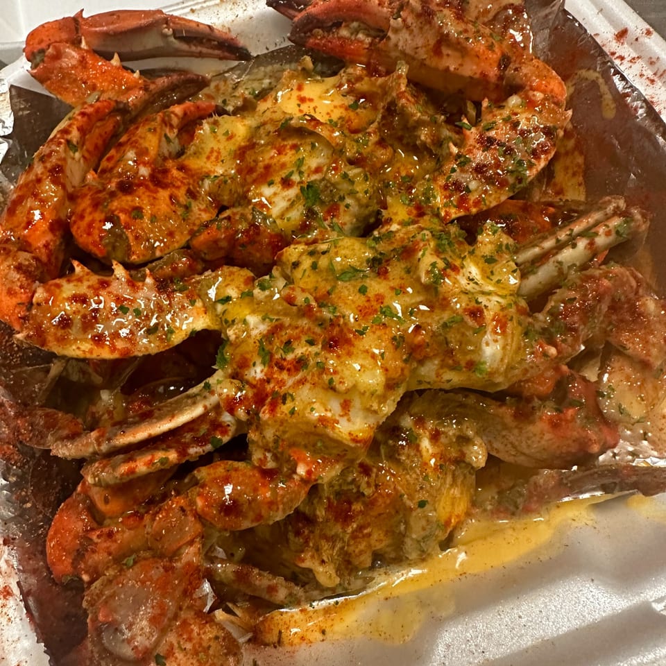 Close-up of seasoned crab legs covered in a rich, creamy sauce with herbs and spices.