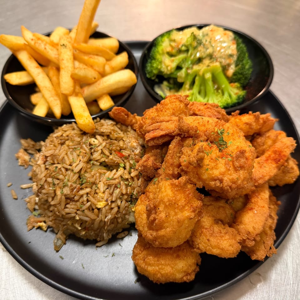 A black plate with fried shrimp, fried rice, french fries, and broccoli with cheese sauce.