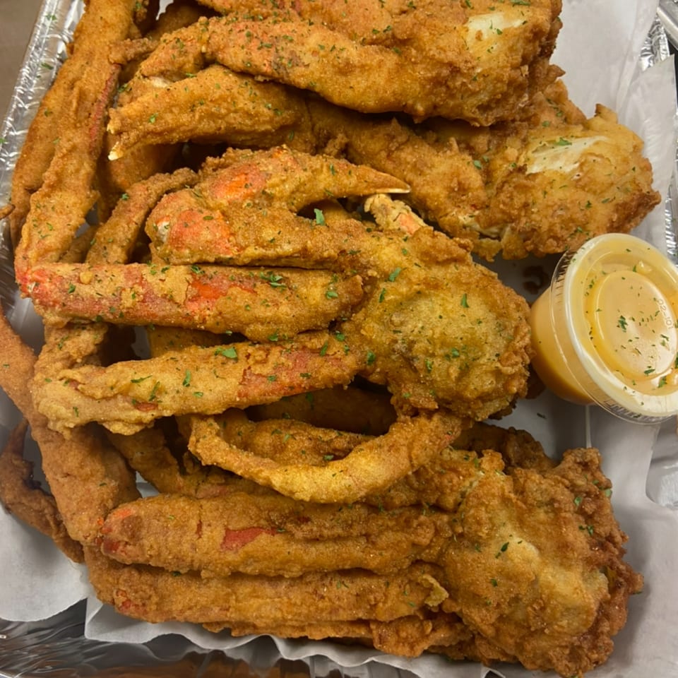 A close-up of golden-brown fried crab legs and seafood, garnished with parsley, next to a dipping sauce.
