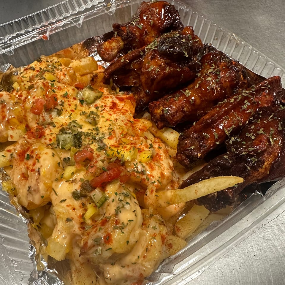 A takeout container with cheesy fries topped with vegetables and barbecue chicken wings.